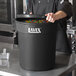 A man in a black chef's coat holding a large black Lavex trash can.