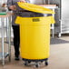 A woman standing next to a Lavex yellow trash can in a room.