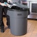 A person in a black apron putting a milk carton in a gray Lavex trash can.