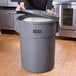 A woman standing in front of a large grey Lavex trash can with a lid.