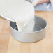 A person pouring dough into a Chicago Metallic round cake pan.