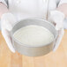 A person in white gloves holding a Chicago Metallic aluminized steel round cake pan.