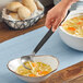 A person using an American Metalcraft wavy stainless steel ladle to serve soup.