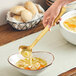 A person using an American Metalcraft hammered gold vintage ladle to serve soup.