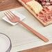 An American Metalcraft hammered bronze cold meat fork on a plate with meat and cheese.