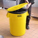 A person putting a plastic bag in a yellow Lavex 44 gallon trash can.