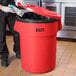A man in a black apron putting a carton of milk in a red Lavex round trash can with a red lid.