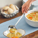 A person using an American Metalcraft stainless steel ladle to pour soup into a bowl.