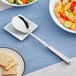 An American Metalcraft stainless steel spoon on a plate next to food.