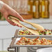 A hand using American Metalcraft gold tongs to serve food at a buffet.