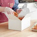 A person in an apron and gloves putting doughnuts into a white barn lunch box.