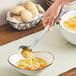 A hand holding an American Metalcraft hammered stainless steel ladle over a bowl of soup.
