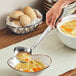 A person using an American Metalcraft hammered stainless steel vintage ladle to pour soup into a bowl.