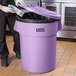 A man in a chef's uniform putting a carton in a Lavex purple trash can.