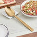 A spoon with a hammered gold handle next to a bowl of rice and vegetables.