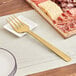 An American Metalcraft hammered gold cold meat fork on a plate of meat.