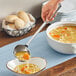 A hand holding an American Metalcraft stainless steel ladle over a bowl of soup.