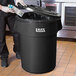 A man in a black apron putting a carton in a black Lavex trash can with a black lid.