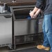 A person putting a glass of ice into a Manitowoc undercounter ice machine.