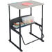 A black Safco AlphaBetter stand up desk with a beige top on it with books and a pencil.