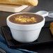 A Tuxton porcelain white china soup cup filled with soup on a table with bread and a knife.