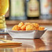 A Tablecraft stainless steel serving basket with fried food on a table.