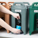 A person using a Cambro slate blue insulated beverage dispenser to fill a cup with water.