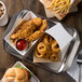 A Tablecraft stainless steel serving tray with fried food including chicken nuggets, a sandwich, and fried onion rings.