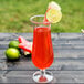 A customizable plastic hurricane glass filled with red liquid with a slice of watermelon and lime on a table.