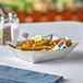A stainless steel Tablecraft serving basket with a bowl of fried food and lemon wedges on a table.