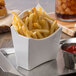 A Tablecraft white melamine fry cup with french fries and ketchup on a table with a glass of soda.