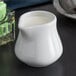 A Tuxton white porcelain creamer pitcher with a liquid in it.