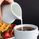 A person pouring milk into a cup of coffee.