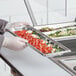 A person in gloves holding a Vollrath stainless steel steam table tray of food.
