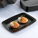 A black Fineline Flairware plastic snack tray with food on it on a table.