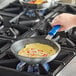 A person cooking food in a Vollrath blue handled non-stick fry pan.