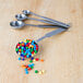 A bowl of Dutch Treat Mini Chocolate Meteor Balls with measuring spoons filled with colorful candy.