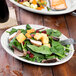 A Fiesta white china oval platter with salad and a fork on a table.