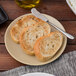 A Tuxton TuxTrendz matte beige coupe plate with a piece of bread on it.