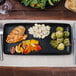 A TuxTrendz Zion matte black china tray with food on a table.