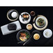 A white bowl with food in it on a table with plates and dishes.