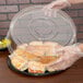 A plastic gloved hand holding a clear plastic Sabert lid over food in a clear plastic container.