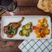 A Tuxton Zion Matte White china tray with grilled chicken and roasted vegetables on a table with a glass of wine.