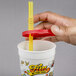 A hand holding a straw in a "Fun at the Fair" souvenir cup with a red lid.