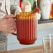 A man pouring liquid from a Cambro Amber plastic pitcher into a glass with a straw.