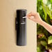 A black wall-mounted cigarette receptacle with a person disposing of a cigarette.