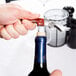 A hand using a Franmara stainless steel corkscrew to open a bottle of wine.