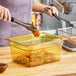 A woman using tongs to place fried chicken in a Carlisle amber plastic food pan.