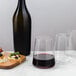 A bottle of red wine and a Stolzle stemless wine glass filled with wine on a table with food.