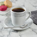 A Schonwald Structure Grey porcelain saucer with a cup of coffee on it with a spoon.